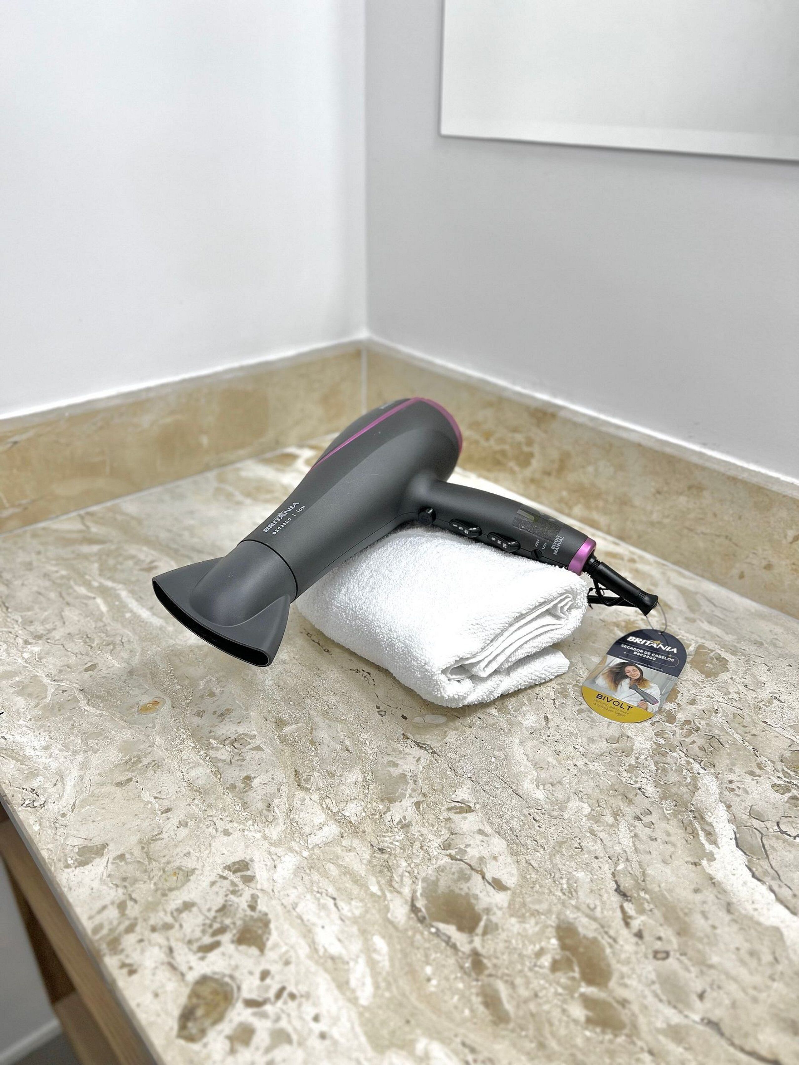 A hair dryer on a marble countertop with a white towel and a bottle of hair product.