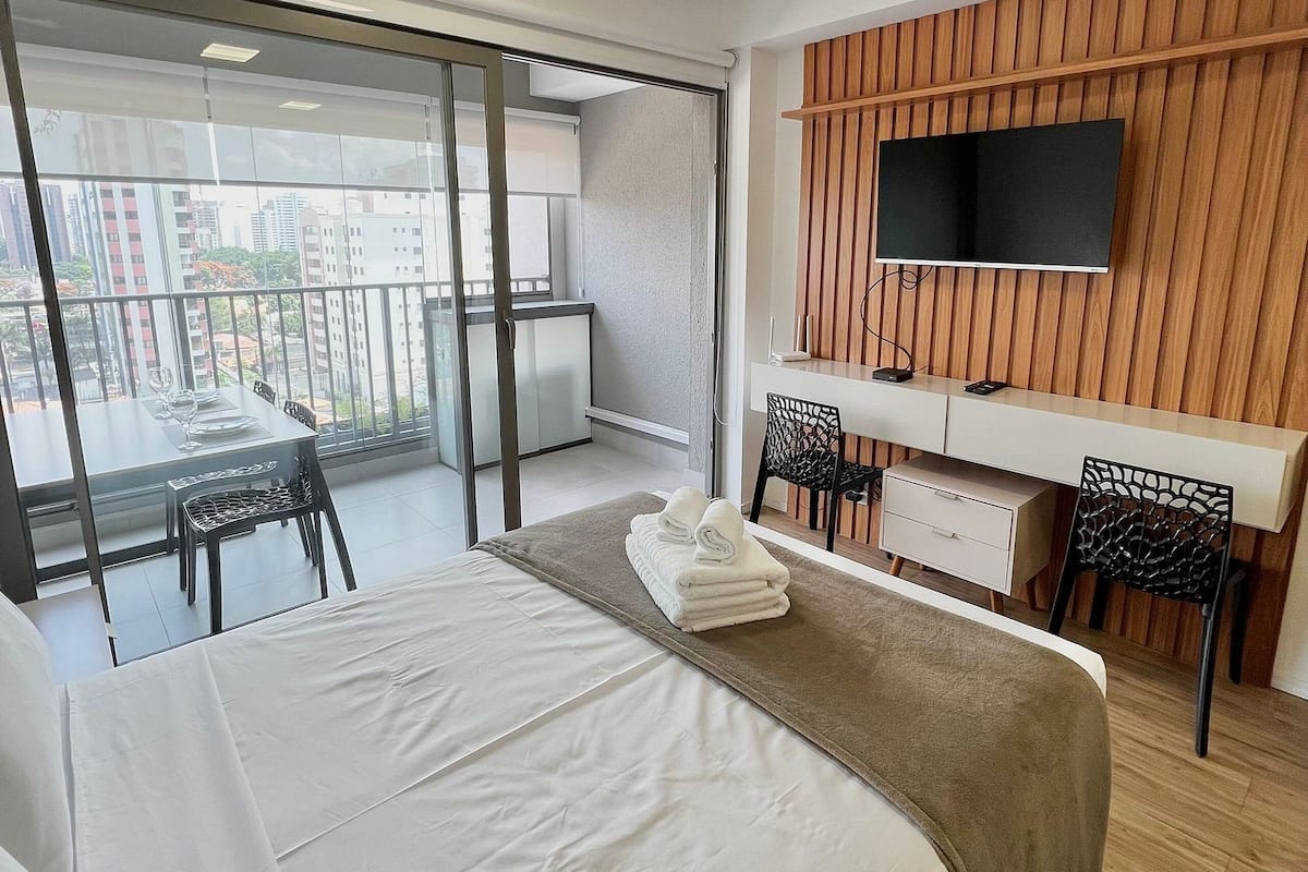 Ein Hotelzimmer mit Bett, Schreibtisch, Fernseher und einem Balkon mit Tisch und Stühlen.