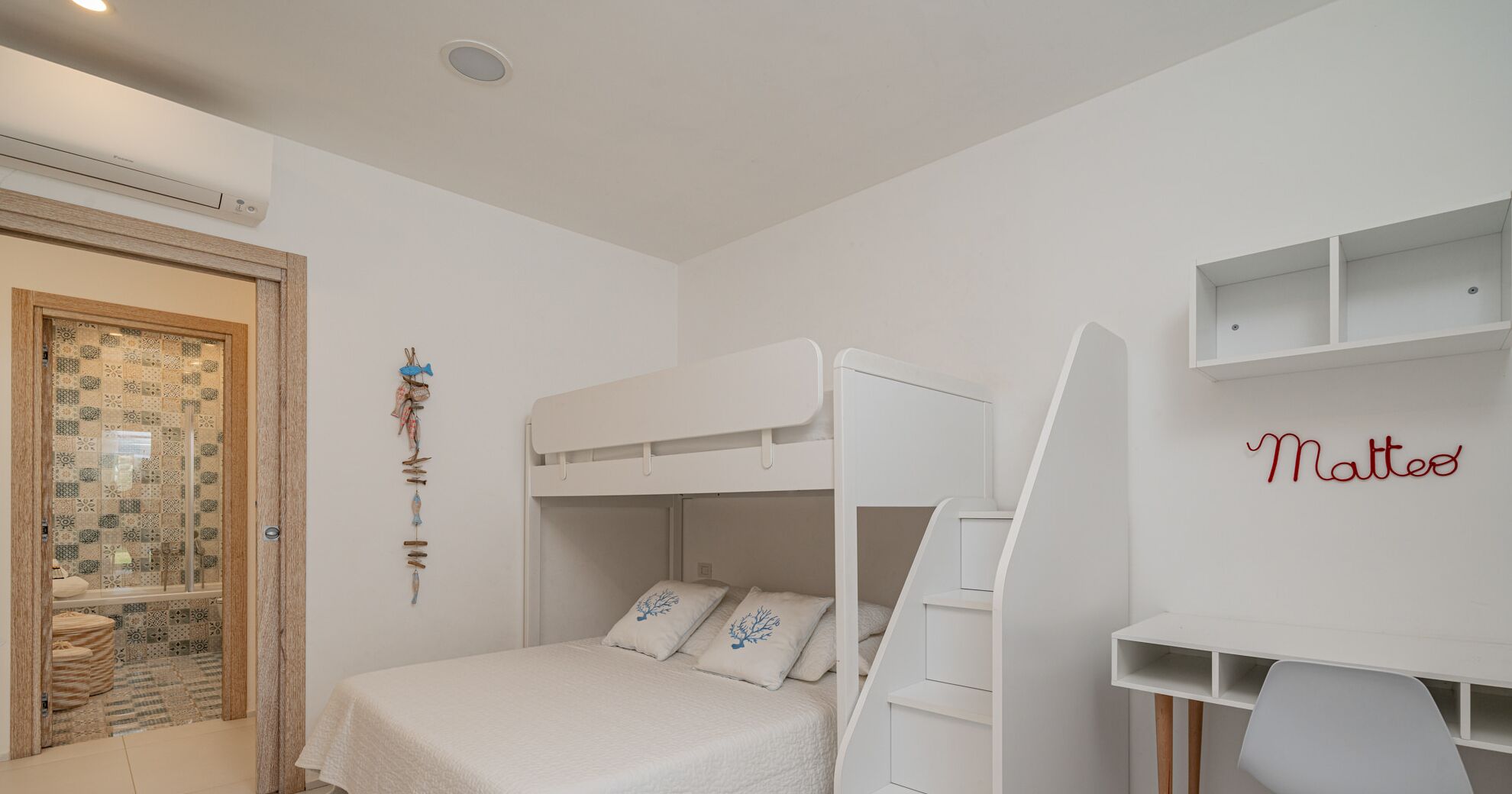 Een slaapkamer met stapelbed, een witte muur en een plank met de naam 'Matteo'.