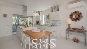 A modern kitchen with white cabinetry, a wooden dining table, and a view of the outdoors. - Villa Elena - Charming Oasis with heated pool (Sardegna)