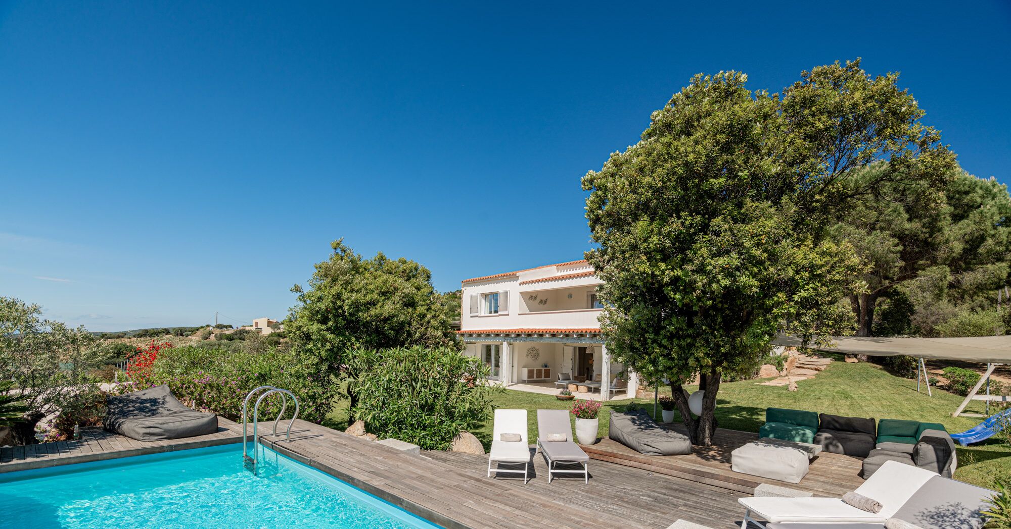 Un espace aménagé au bord de la piscine, avec une terrasse en bois, deux chaises longues et une petite table.