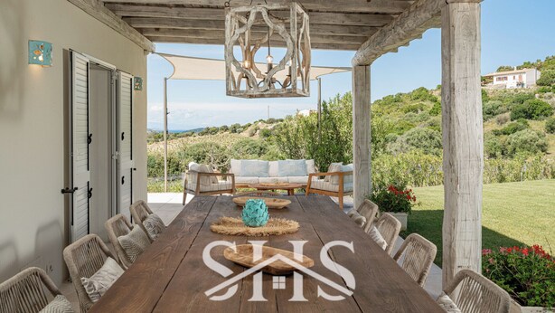 A covered outdoor dining area with a wooden table and chairs, a hanging light fixture, and a view of a hillside. - Villa Elena - Charming Oasis with heated pool (Sardegna)