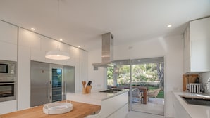 A modern kitchen with built-in appliances, a large island, and a glass door leading to an outdoor area. - Villa Elena - Charming Oasis with heated pool (Sardegna)