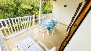 Un balcon agrémenté d’une table et de chaises, entouré d’une clôture blanche et d’une végétation luxuriante.