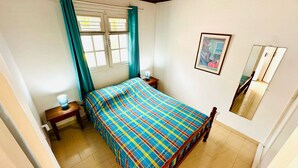 Une chambre à coucher comprenant un lit, une table de chevet, une lampe, une fenêtre avec des rideaux, un tableau et un miroir.