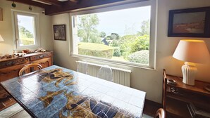 A dining area with a large table, wooden beams, a window with a view, and a lamp.