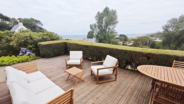 A wooden deck with outdoor furniture including a sofa, two chairs, a small table, and a larger table.