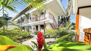 A modern two-story building with a balcony, surrounded by lush greenery and a concrete pathway. - Olinca Boutique Hotel (Cahuita)