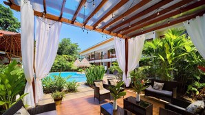 A covered outdoor area with a pool, wicker furniture, and potted plants. - Olinca Boutique Hotel (Cahuita)