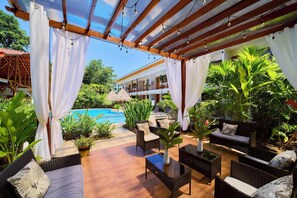 A covered outdoor area with a pool, wicker furniture, and potted plants. - Olinca Boutique Hotel (Cahuita)