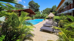 A pool area with lounge chairs, a thatched umbrella, and tropical vegetation. - Olinca Boutique Hotel (Cahuita)