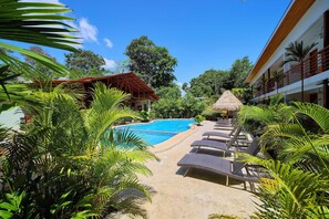 A pool area with lounge chairs, a thatched umbrella, and tropical vegetation. - Olinca Boutique Hotel (Cahuita)