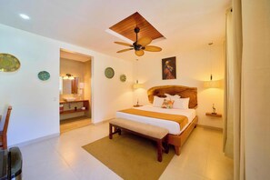 Habitación de hotel con cama, ventilador de techo, cabecero de madera, mesita de noche y espejo, además de una ventana con cortinas.