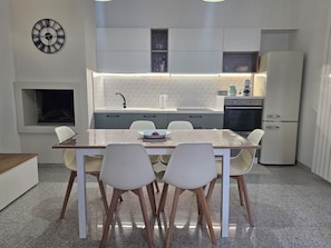 A modern kitchen with a dining table, chairs, a built-in oven, and a refrigerator.