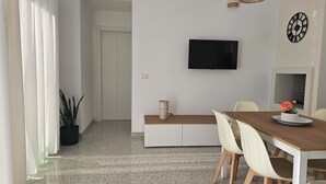 A modern dining area with a wooden table, white chairs, a TV mounted on the wall, and a potted plant. - Retrò holiday home- Pandorea (Sava)
