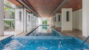Une piscine à l’eau claire, entourée de murs de verre et surmontée de poutres en bois.