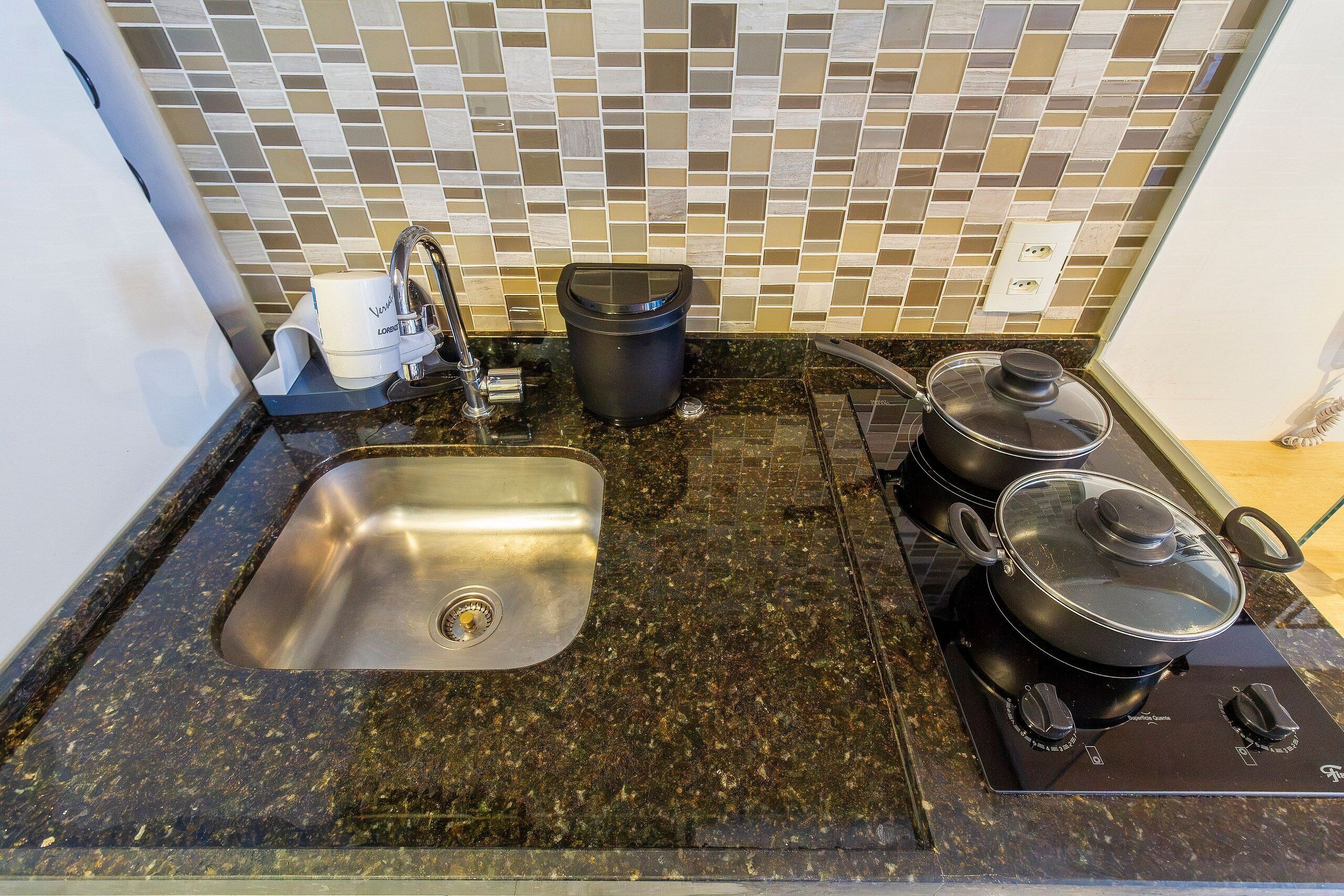 Una cocina con un lavamanos de acero inoxidable, un cubo de basura negro y una estufa con ollas.