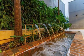A water feature with multiple streams, surrounded by lush greenery and a tiled walkway.