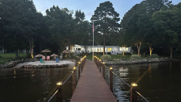 A wooden bridge over a body of water with a row of lights along the sides. There are trees and a building in the background. - LAKEFRONT GARDEN COTTAGE- beach, screened porch, dock, private, amazing views (Lake Norman of Catawba)