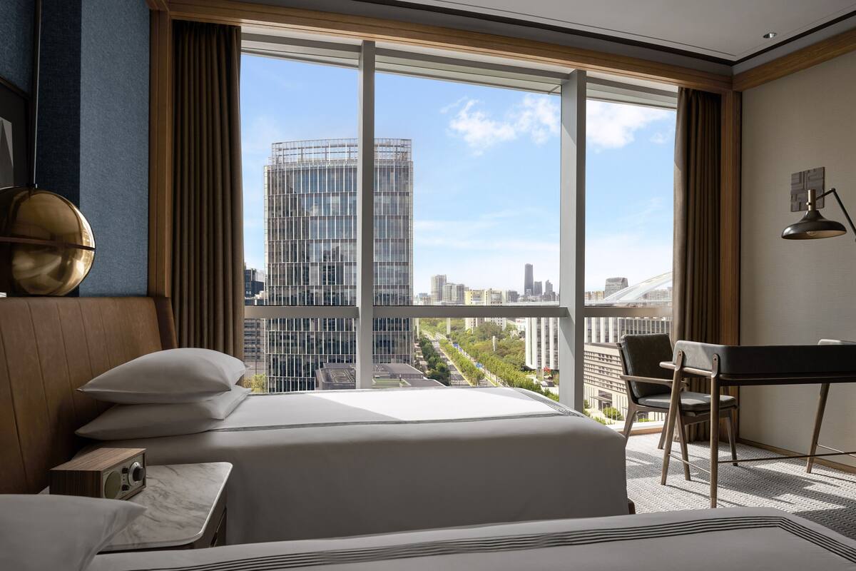 A hotel room with a large window, a bed, a desk, and a chair.