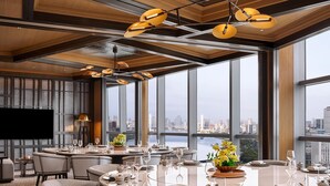 Un'area pranzo moderna con tavoli rotondi, sedie e vista sulla città attraverso ampie finestre.