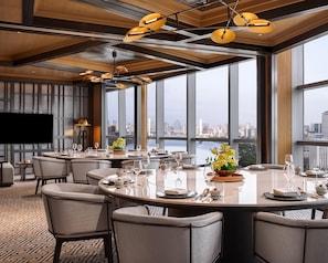Een moderne eetruimte met ronde tafels, stoelen en uitzicht over de stad door grote ramen.