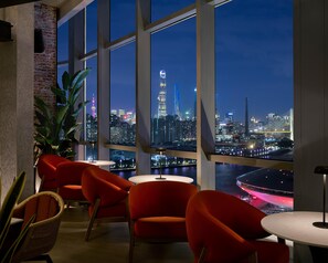 Ein modernes Interieur mit großen Fenstern, roten Stühlen, einem runden Tisch und Blick auf eine nächtliche Skyline.