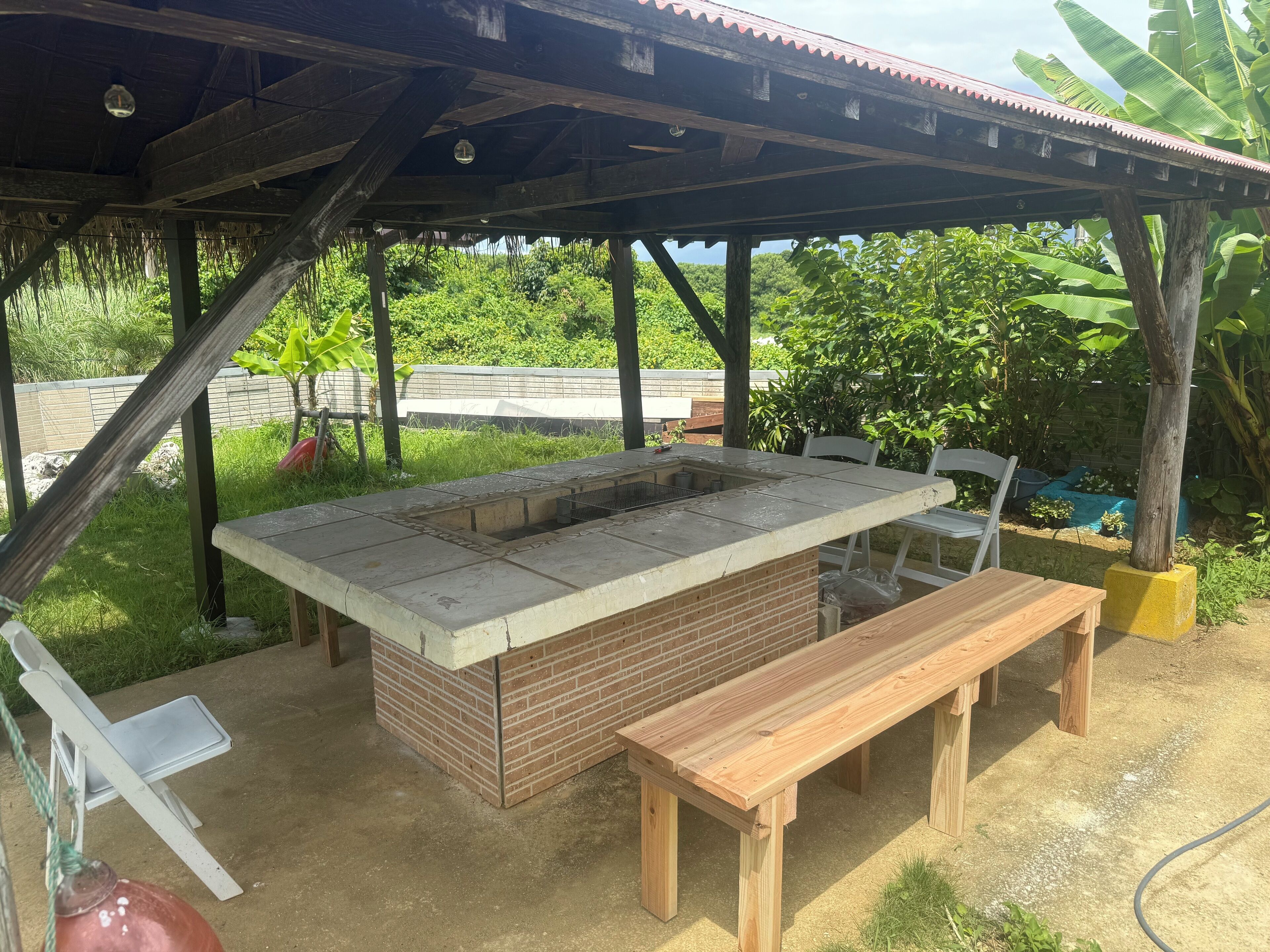 An outdoor barbecue area with a brick grill, wooden benches, and a covered shelter.