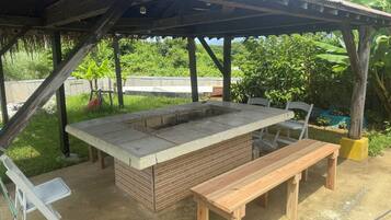 An outdoor barbecue area with a brick grill, wooden benches, and a covered shelter.