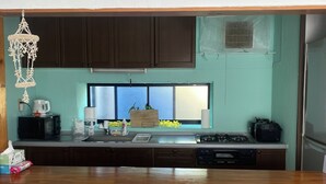 A kitchen with a wooden countertop, three stools, a hanging light fixture, and cabinets.