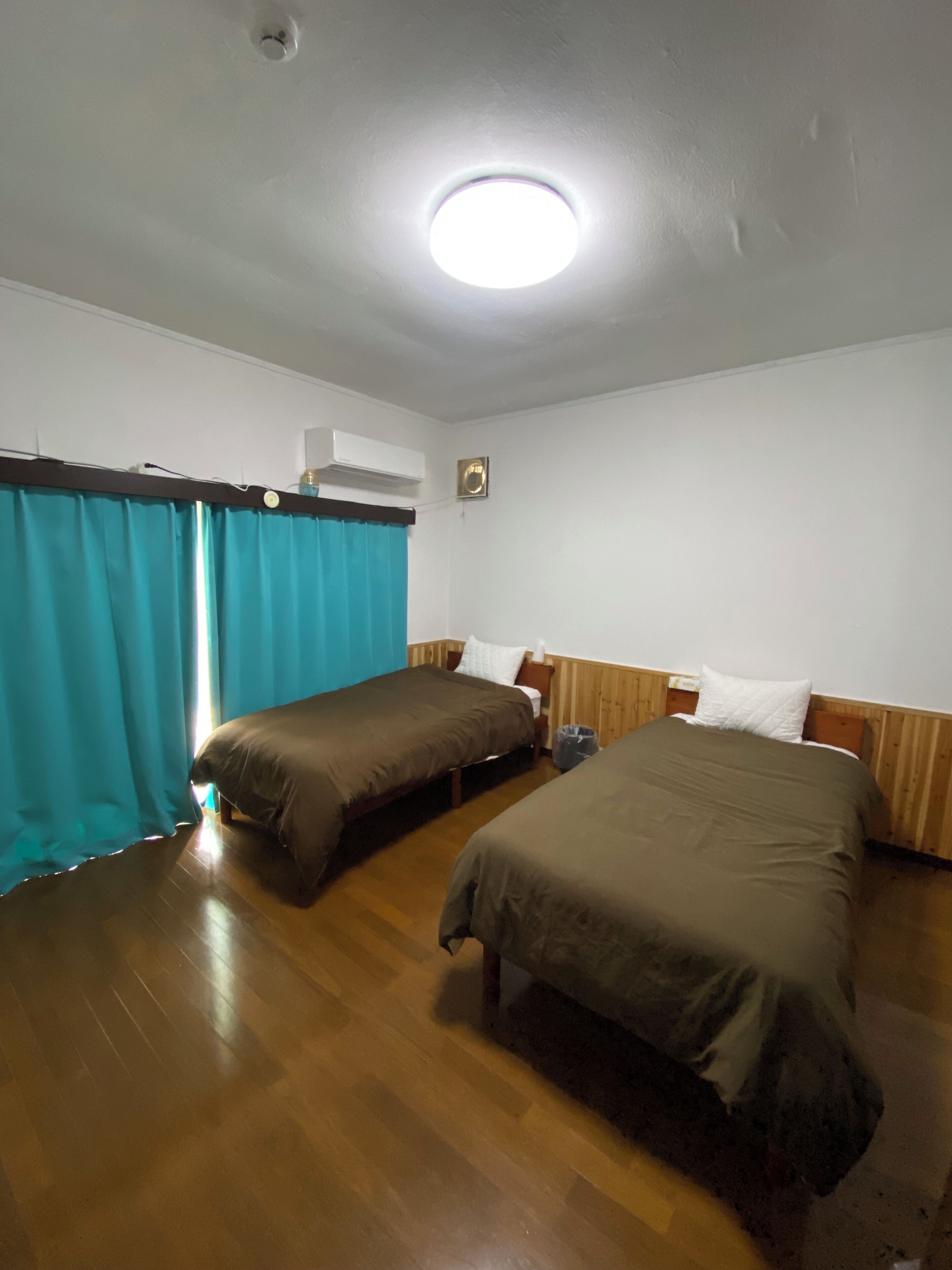 Een kamer met twee bedden, een plafondlamp, een airconditioning en een houten vloer.