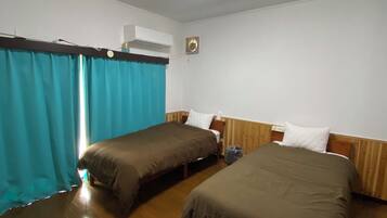 Een kamer met twee bedden, een plafondlamp, een airconditioning en een houten vloer.