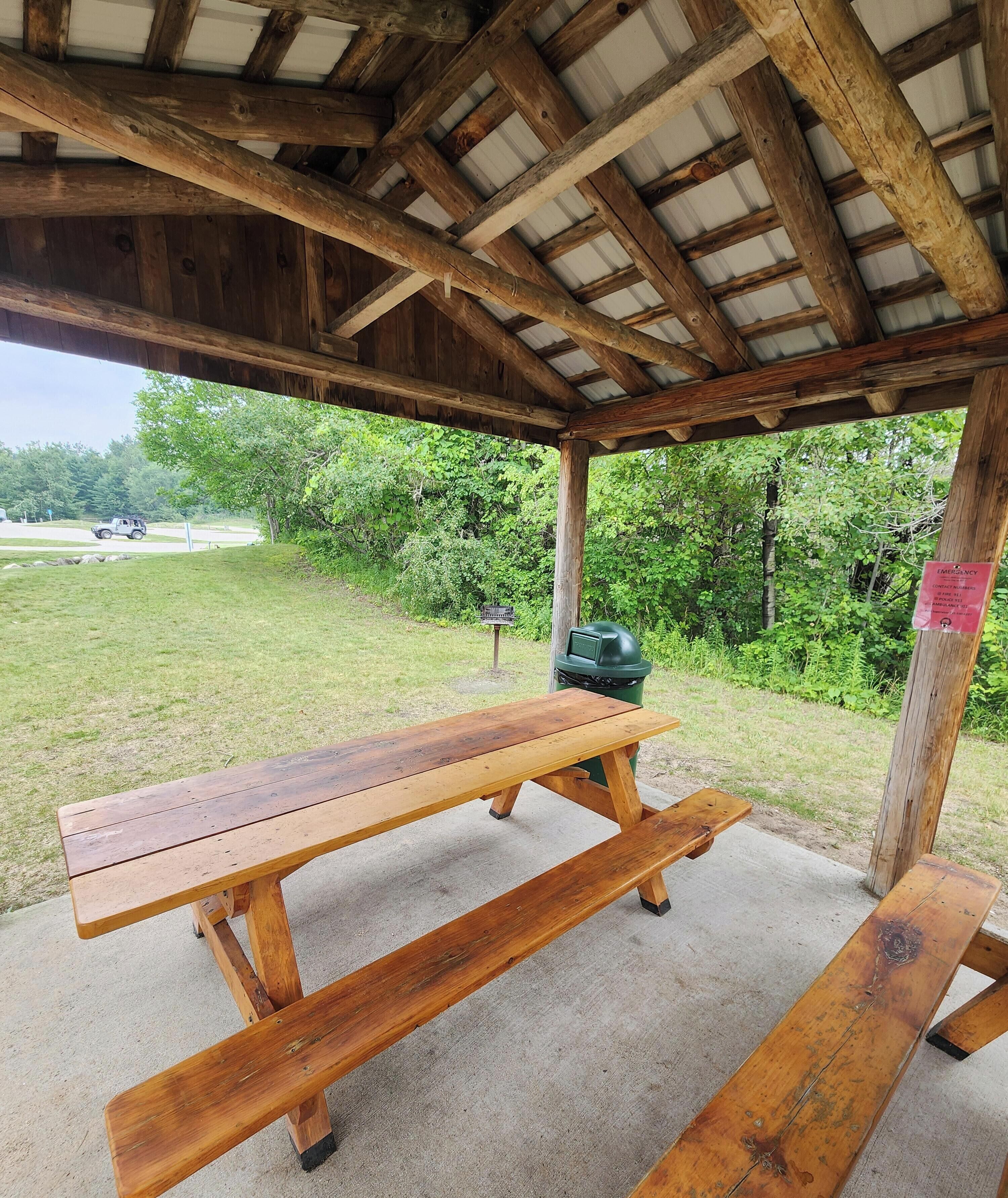 Un espace pique-nique abrité, équipé de bancs en bois et d’un barbecue.