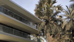 Un bâtiment moderne doté de nombreux balcons, avec de luxuriants palmiers au premier plan.
