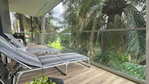 Un balcon avec deux chaises longues, un pot de fleurs et une vue sur des palmiers et une végétation luxuriante.
