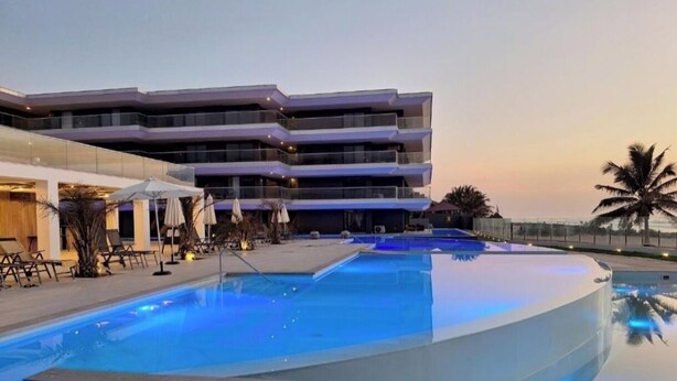 Un hôtel moderne doté d’une piscine, de chaises longues et d’un espace abrité avec des parasols.