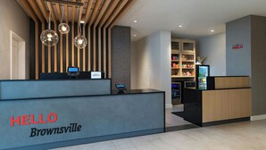 A reception desk with a sign reading "HELLO Brownsville," a wooden slat ceiling, and a reception area with a counter and shelves in the background. - Towneplace Suites By Marriott Brownsville (Brownsville)