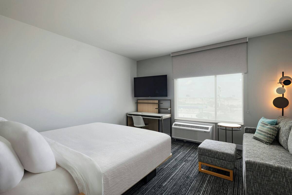 A hotel room with a bed, a desk, a TV, a couch, and a window with a city view.