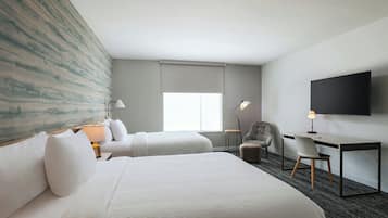 Habitación de hotel con dos camas, un escritorio, una silla, un televisor y una ventana con vistas.