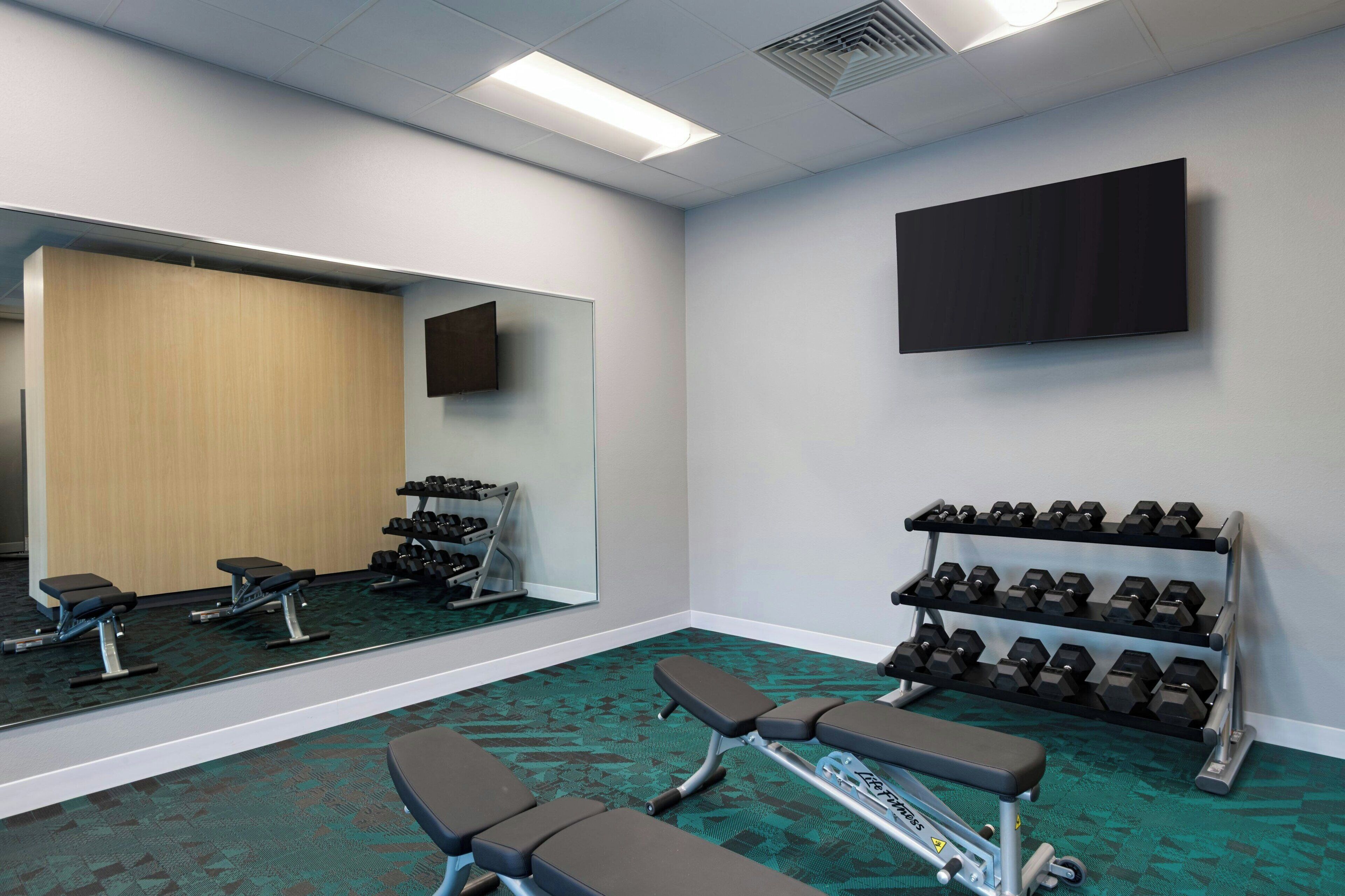 A gym with exercise equipment, a bench, a mirror, and a TV on the wall.