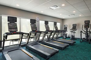 Un gimnasio con cintas de correr, elípticas y bicicletas estáticas, equipado con pantallas digitales y un reloj en la pared.