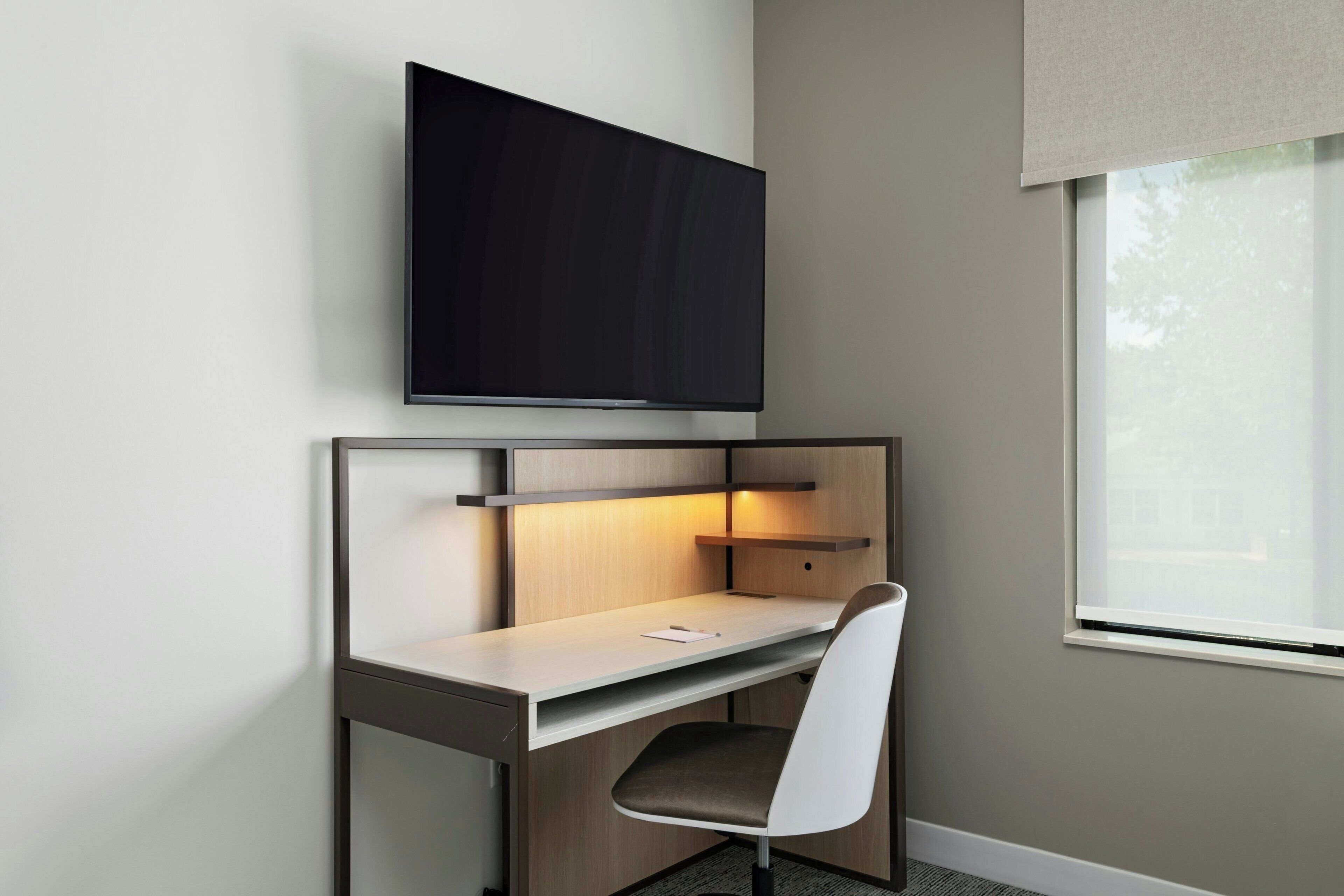 A modern hotel room with a desk, chair, and a flat-screen TV mounted on the wall.