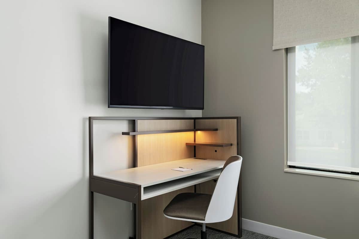 A modern hotel room with a desk, chair, and a flat-screen TV mounted on the wall.