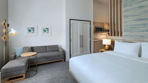 Habitación de hotel con cama, sofá, mesita, armario, microondas y un cuadro en la pared.