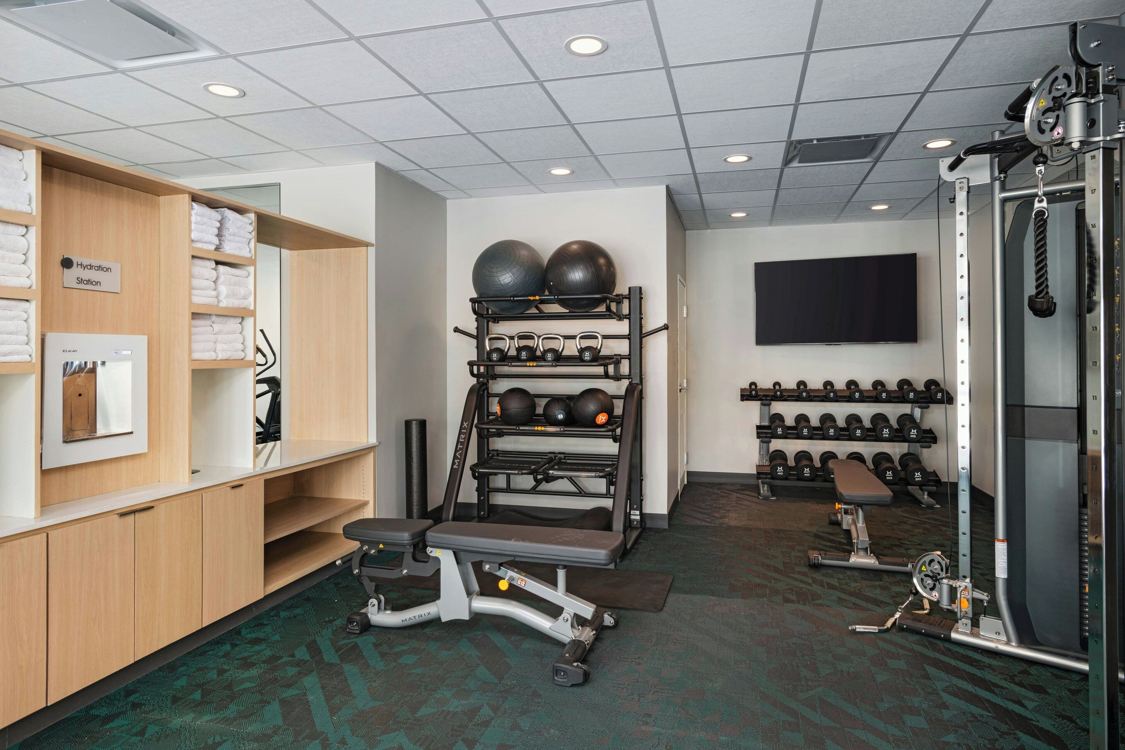 A gym with exercise equipment, a hydration station, and a television on the wall.