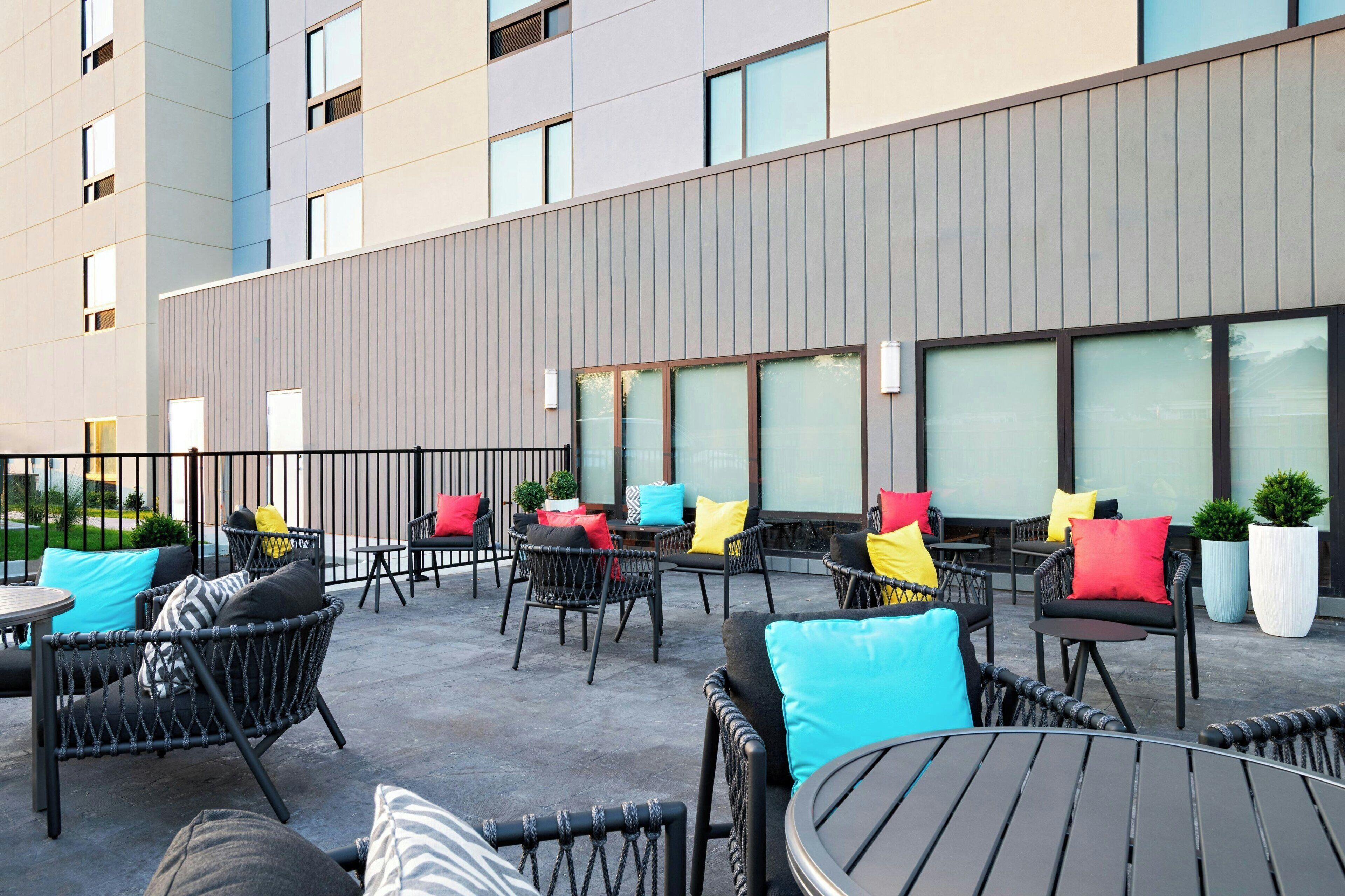 An outdoor patio area with wicker furniture, colorful cushions, and large windows.