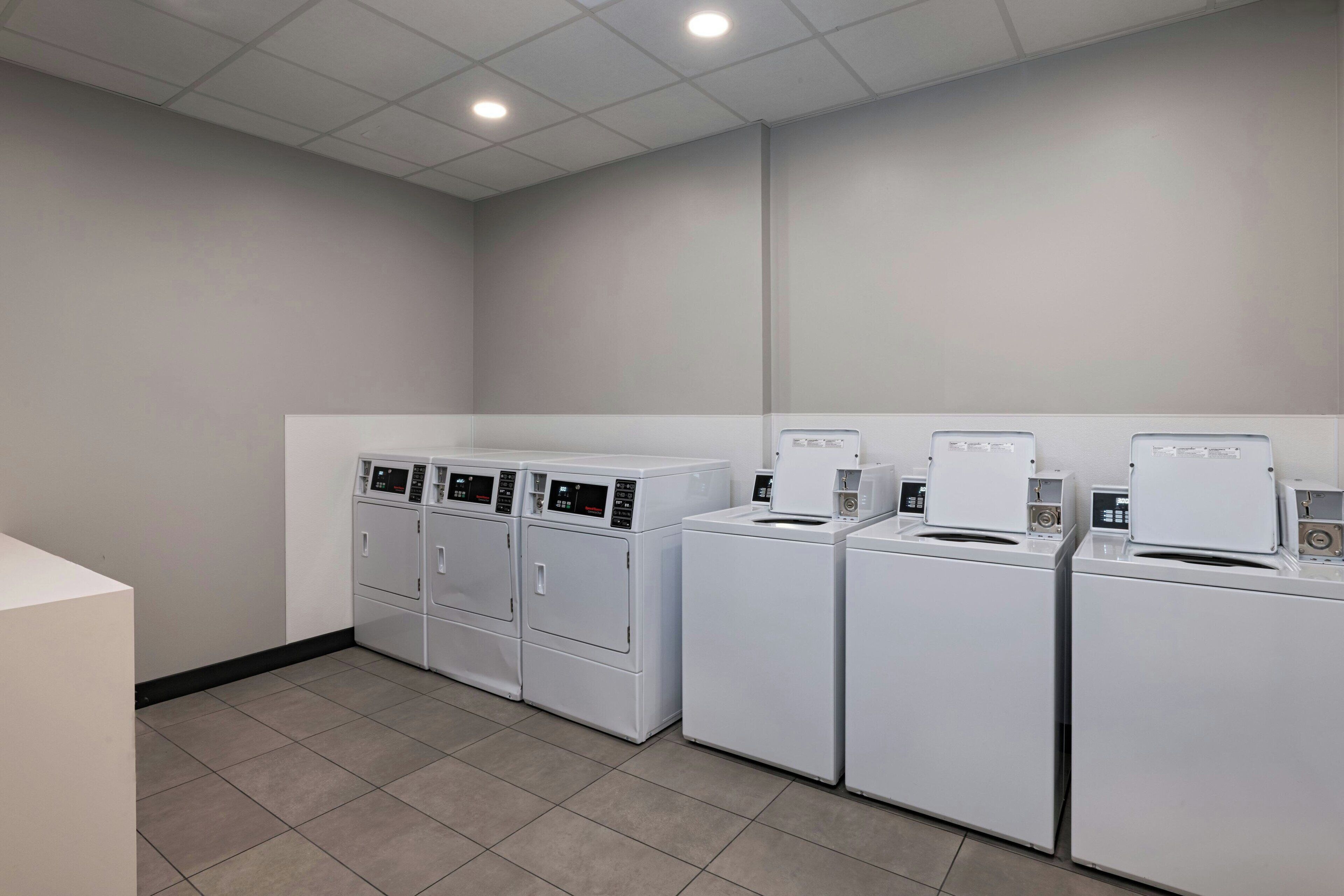 A laundry room with four white front-loading washing machines and two stacked dryers.