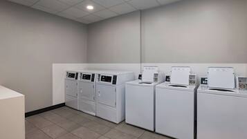 A laundry room with four white front-loading washing machines and two stacked dryers.