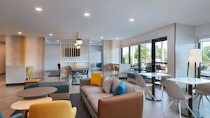 Un moderno vestíbulo de hotel con un sofá, sillas, mesas y una zona de comedor.