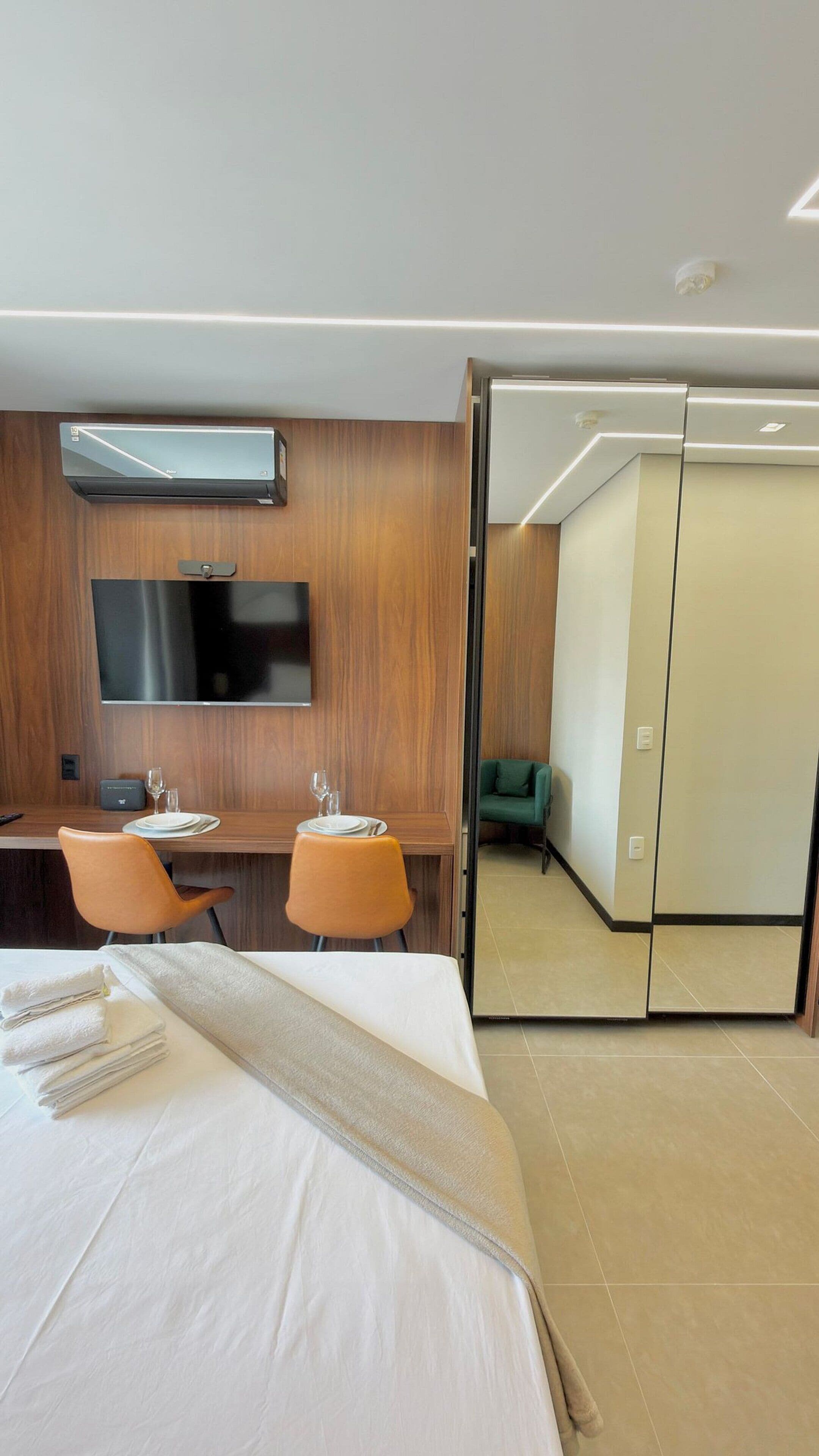A hotel room with a bed, a desk with chairs, a flat-screen TV, and a sliding door leading to a bathroom.